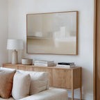 A minimalist living room with a light wood sideboard, books, lamp, beige sofa with cushions, and the Soft Layers Canvas Art - Horizontal in soft neutral tones enhancing the serene, neutral palette.