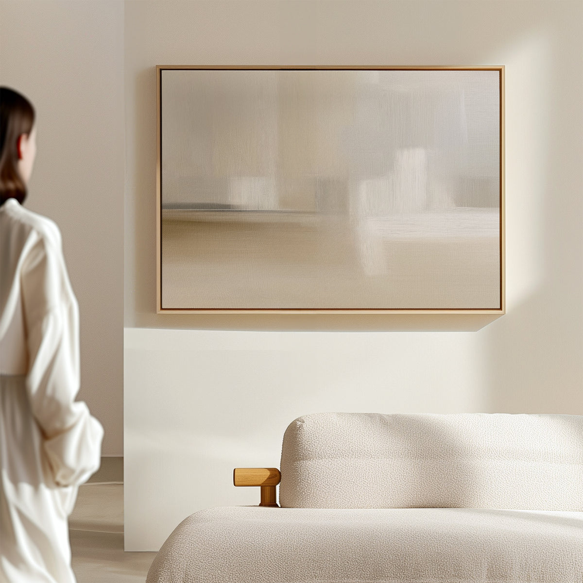 A person in a white shirt stands in a bright, minimal room with a beige sofa and the Soft Layers Canvas Art - Horizontal, featuring neutral tones, displayed on the wall.