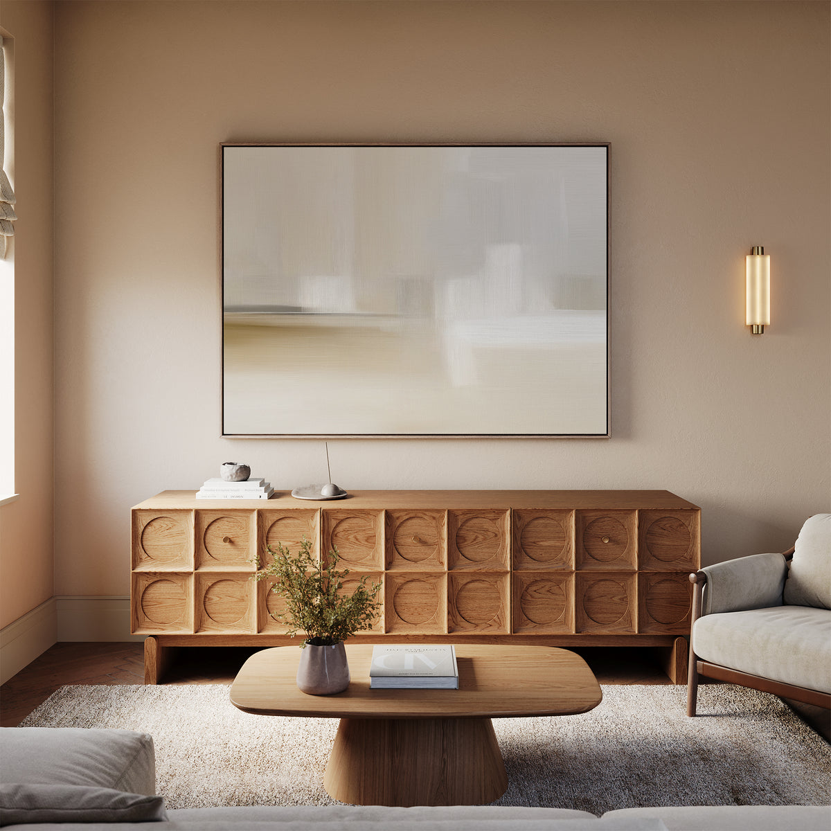 A modern living room with a neutral palette features a wooden sideboard with circular patterns, the Soft Layers Canvas Art - Horizontal above it, a coffee table decorated with flowers, a sofa, and a soft wall-mounted light fixture.