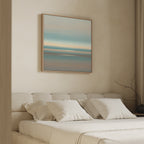 A minimalist bedroom features a beige upholstered bed with white bedding and pillows. Above the bed hangs the Soft Tide Layers Canvas Art - Square, showcasing calming blue, beige, and peach tones. A bare branch decorates the right nightstand.