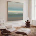 A modern, minimalist living room featuring a white leather lounge chair and ottoman, a geometric wooden side table with lamp, and Soft Tide Layers Canvas Art - Square in soothing blue, green, and orange tones adorning the wall.