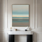A minimalist room features a marble console table with decor accents and the Soft Tide Layers Canvas Art - Vertical, showcasing calming blue, beige, and peach hues on a light-paneled wall—perfect for tranquil home decor.