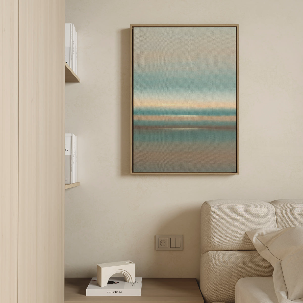 A modern living room features a light beige sofa, built-in wooden shelf with books and a small decor object, and the Soft Tide Layers Canvas Art - Vertical as calming coastal wall art in blue, teal, and beige on a cream wall.