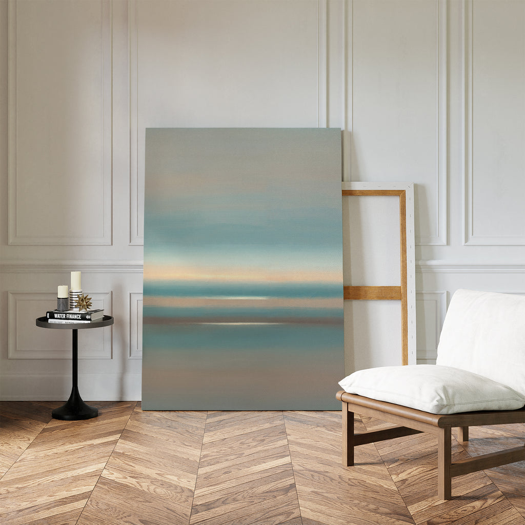 A minimalist room featuring chevron wood floors, a white cushioned chair, a black round table with candles and books, and the Soft Tide Layers Canvas Art - Vertical leaning against a white paneled wall for tranquil home decor.