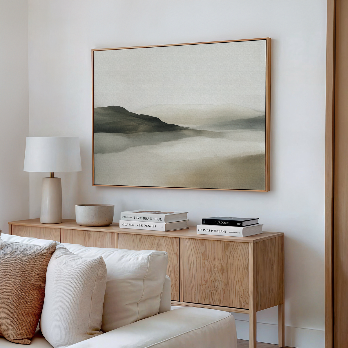 A modern living room with a light wood sideboard, minimalist decor, books, a white table lamp, and the Soft Valley Canvas Art – Horizontal in soft earthy tones hanging above.