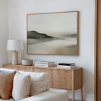 A modern living room with a light wood sideboard, minimalist decor, books, a white table lamp, and the Soft Valley Canvas Art – Horizontal in soft earthy tones hanging above.