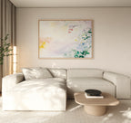 A modern living room with a light beige sectional sofa, wooden coffee table, light carpet, and the Spring Reverie Canvas Art - Horizontal featuring pastel floral hues displayed above the sofa.