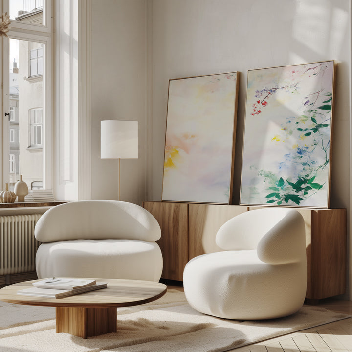 A modern living room with two rounded white armchairs, a low wooden coffee table, and a sideboard displays the Spring Reverie - Set of 2 watercolor wall art. These floral pieces add charm beneath a window filled with natural light.
