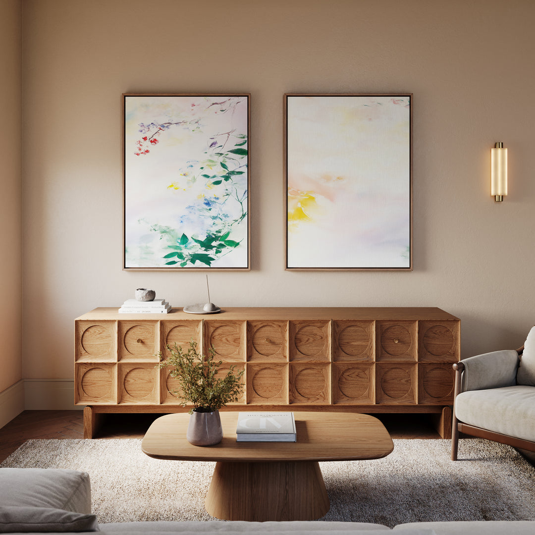 A minimalist living room with a wooden sideboard, coffee table, and light gray armchair. Above the sideboard hang Spring Reverie - Set of 2 watercolor floral paintings; a wall sconce and vase with flowers add to the serene scene.