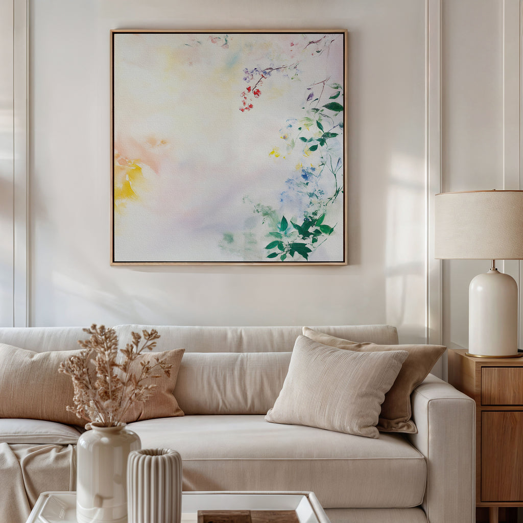 A neutral-toned living room features a beige sofa, cream pillows, and a white lamp on the side table. Above the sofa hangs the Spring Reverie Canvas Art - Square, while dried flowers in a vase accent the coffee table.
