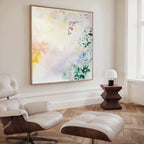 A modern living room with a white leather lounge chair and ottoman, dark wood side table with a white lamp, and the "Spring Reverie Canvas Art - Square," a large botanical watercolor print, displayed on the wall.