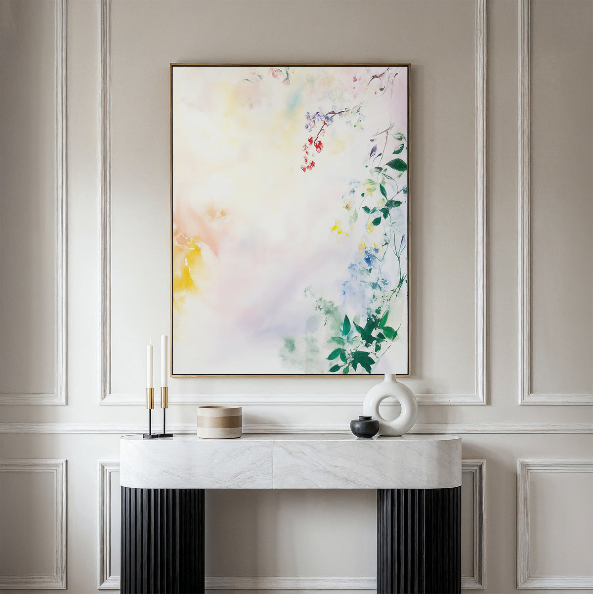 A console table with decorative objects stands against a paneled wall. Above it hangs the Spring Reverie Canvas Art - Vertical, featuring soft pastel colors and hints of botanical shapes in an abstract watercolor style.