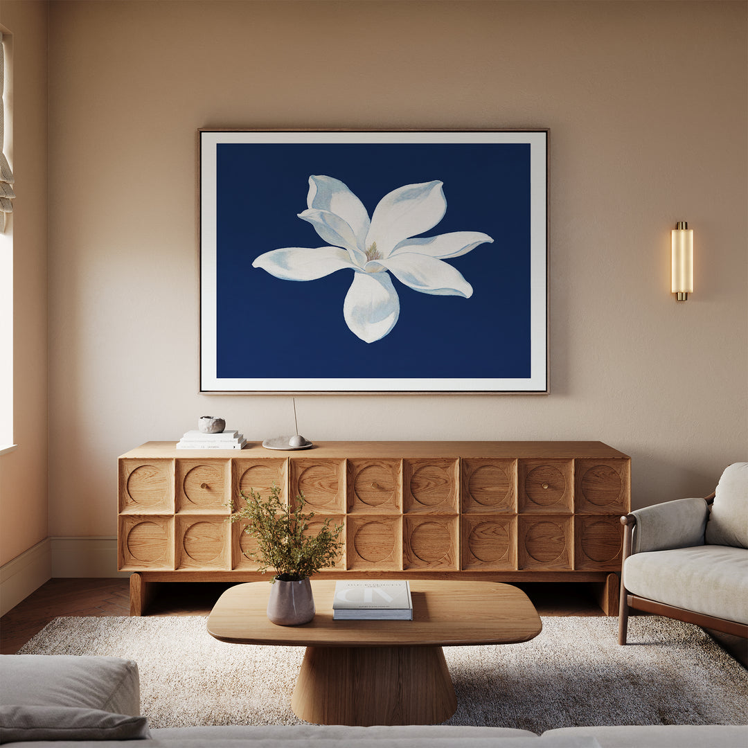 A modern living room featuring neutral walls, a light wood sideboard, beige sofa, wooden coffee table, and the Starlit Magnolia Canvas Art - Horizontal as contemporary wall art above the sideboard.