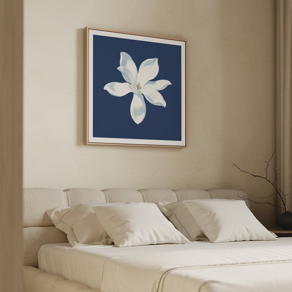 A minimal bedroom with a beige bed and pillows, light walls, and the Starlit Magnolia Canvas Art - Square featuring a white magnolia on a dark blue background hanging above the bed.