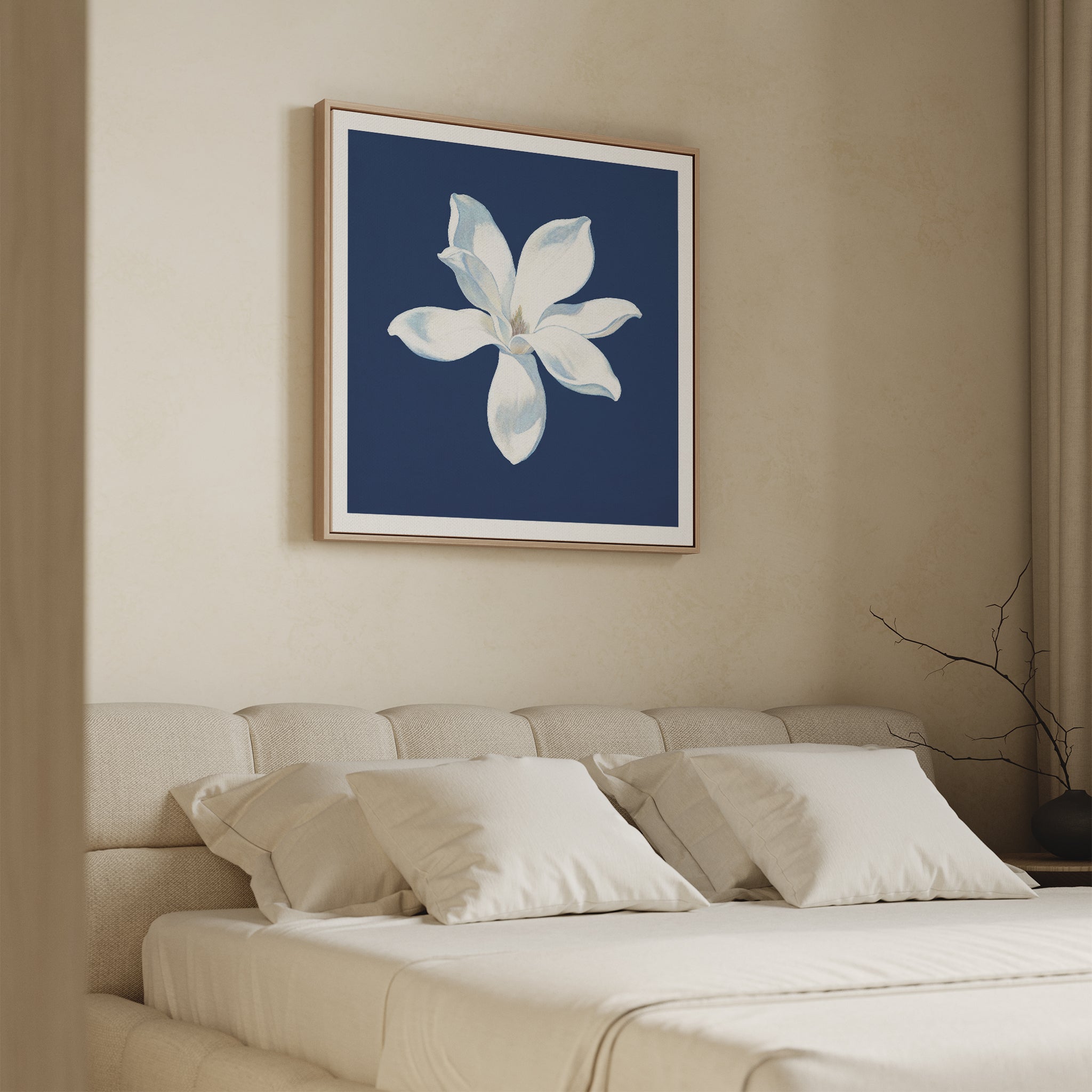A minimal bedroom with a beige bed and pillows, light walls, and the Starlit Magnolia Canvas Art - Square featuring a white magnolia on a dark blue background hanging above the bed.