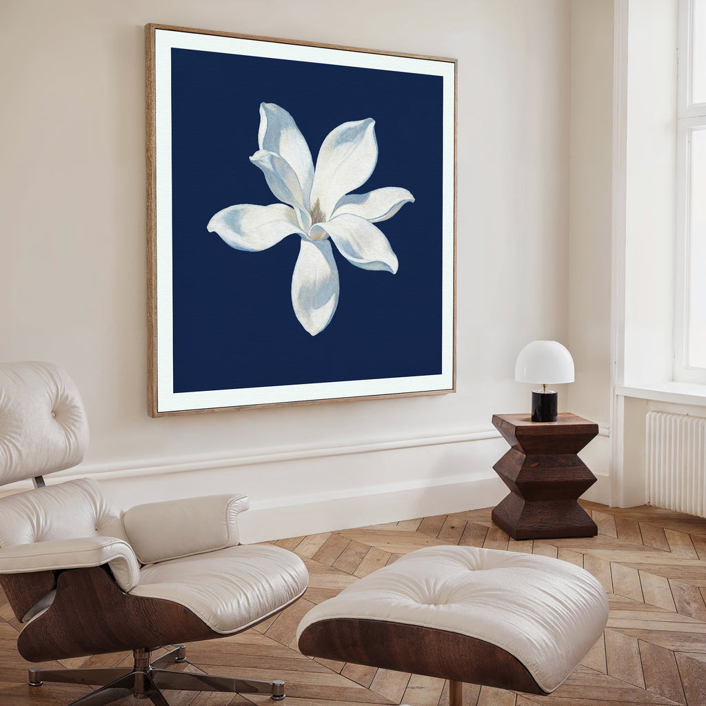 A modern living room featuring a white lounge chair and ottoman, a side table with lamp, and the Starlit Magnolia Canvas Art - Square as striking wall decor, creating an elegant Nordic Park-inspired atmosphere.