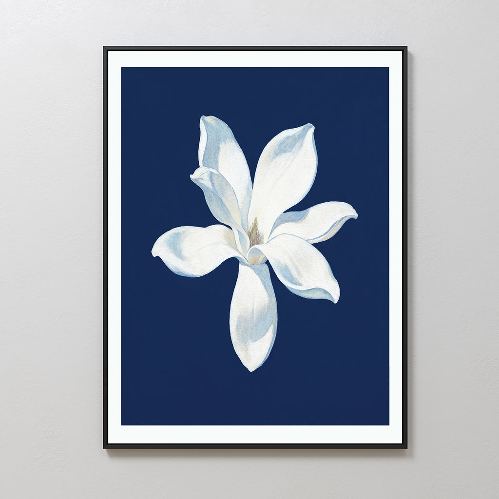 The Starlit Magnolia Canvas Art - Vertical showcases a single white magnolia with soft petals on a deep blue background, framed and displayed on a light gray wall—an ideal piece of contemporary wall art.
