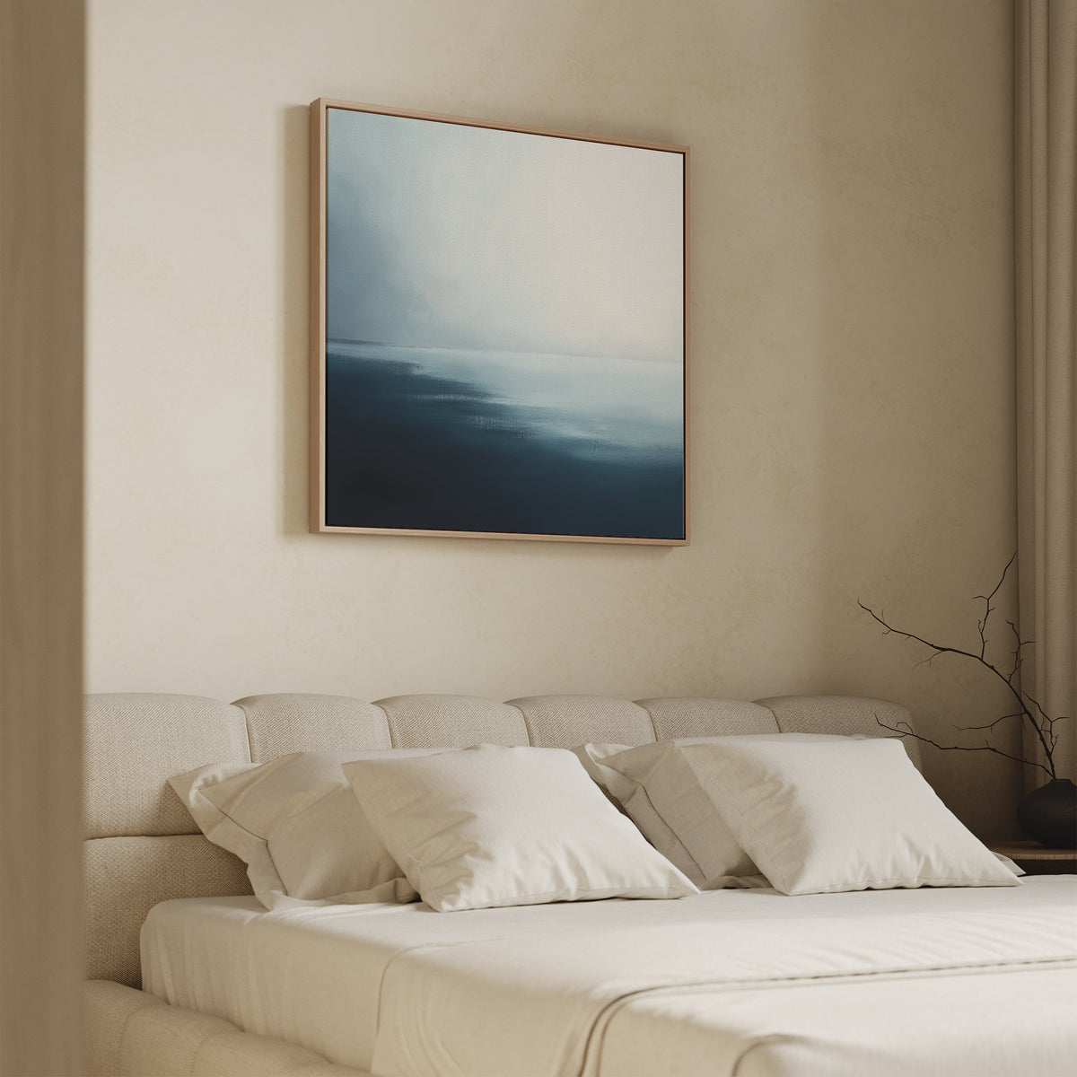A minimalist bedroom with a beige upholstered bed and white bedding features the Steel Harbor Mist Canvas Art - Square above the bed, showcasing abstract blue and gray patterns. A bare branch sits on the bedside table.