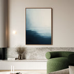 A modern living room with a green curved sofa, Steel Harbor Mist Canvas Art - Vertical featuring abstract blue and white hues, a marble ledge with dried flowers in a glass vase, and a round wall light.