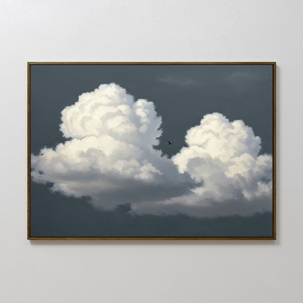 The Storm Passage Canvas Art - Horizontal features two fluffy white clouds on a dark gray sky with a small bird silhouette, framed in thin brown wood for a Nordic Park look, shown hanging on a plain white wall.