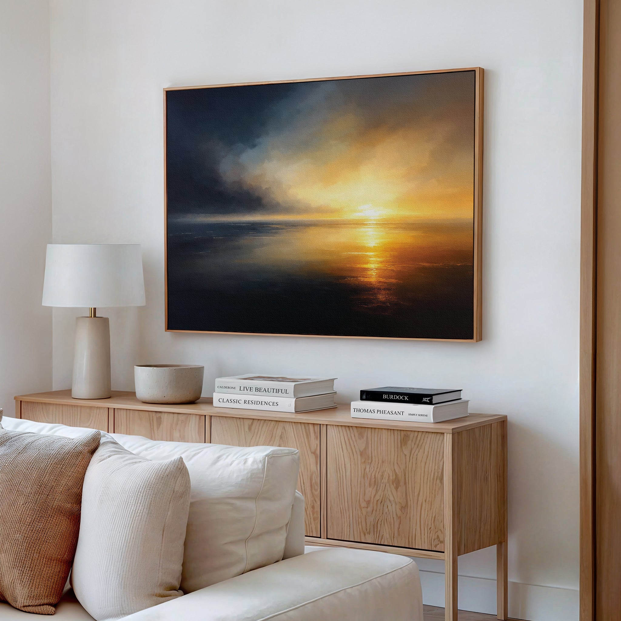 A minimalist living room features a light wood sideboard with books, a lamp, and a bowl. Above it hangs the Storm's Edge Canvas Art - Horizontal, adding drama, while a beige couch is partially visible in the foreground.