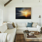 A cozy living room features a white sectional, neutral pillows, rustic wood coffee table, and the Storm's Edge Canvas Art - Horizontal of a sunset seascape mounted on a white shiplap wall. Sunlight pours in from the left window.