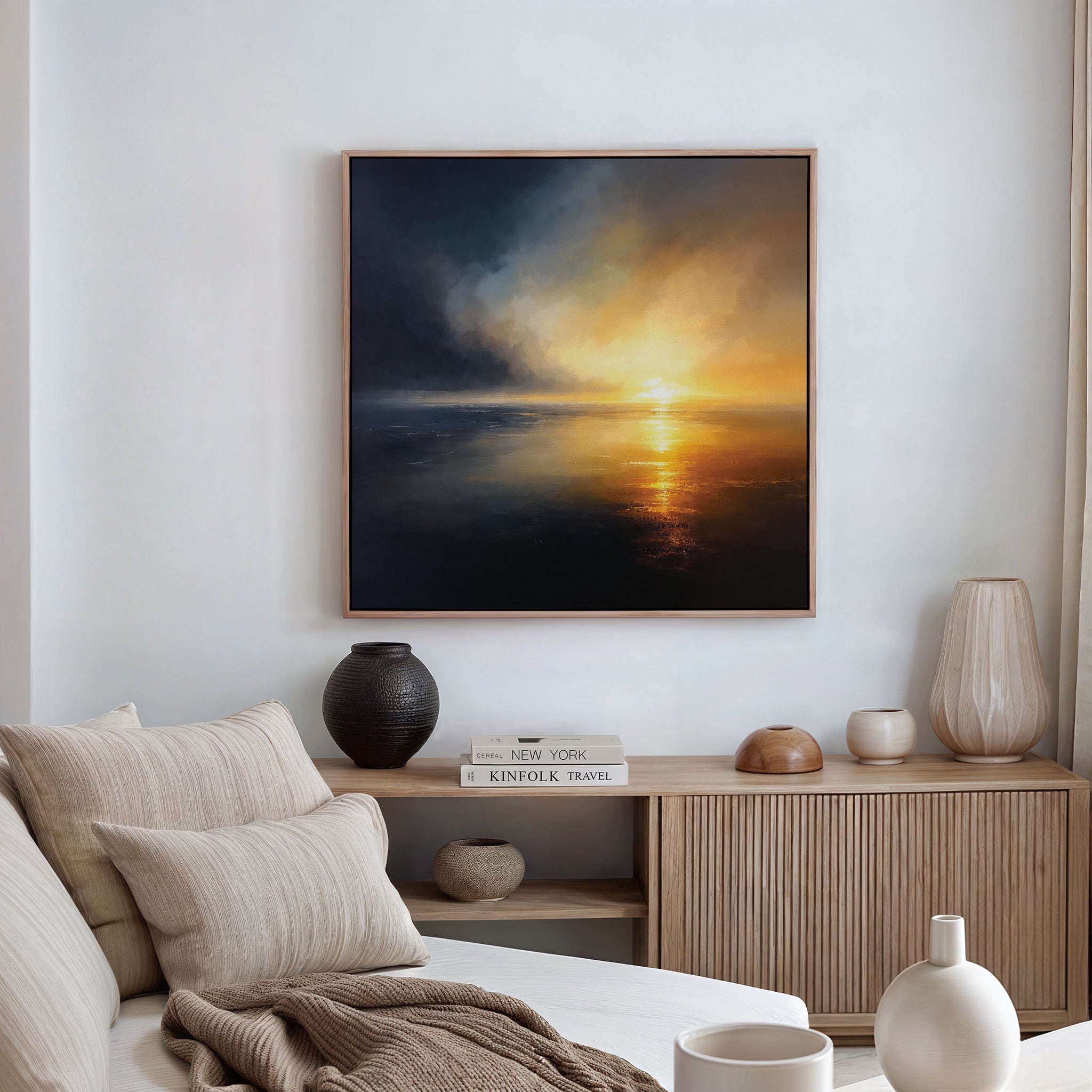 A modern living room with a beige sofa, neutral cushions, a wooden cabinet, and Storm's Edge Canvas Art - Square featuring a dramatic sunset over water as the centerpiece. Natural light enhances the serene atmosphere.