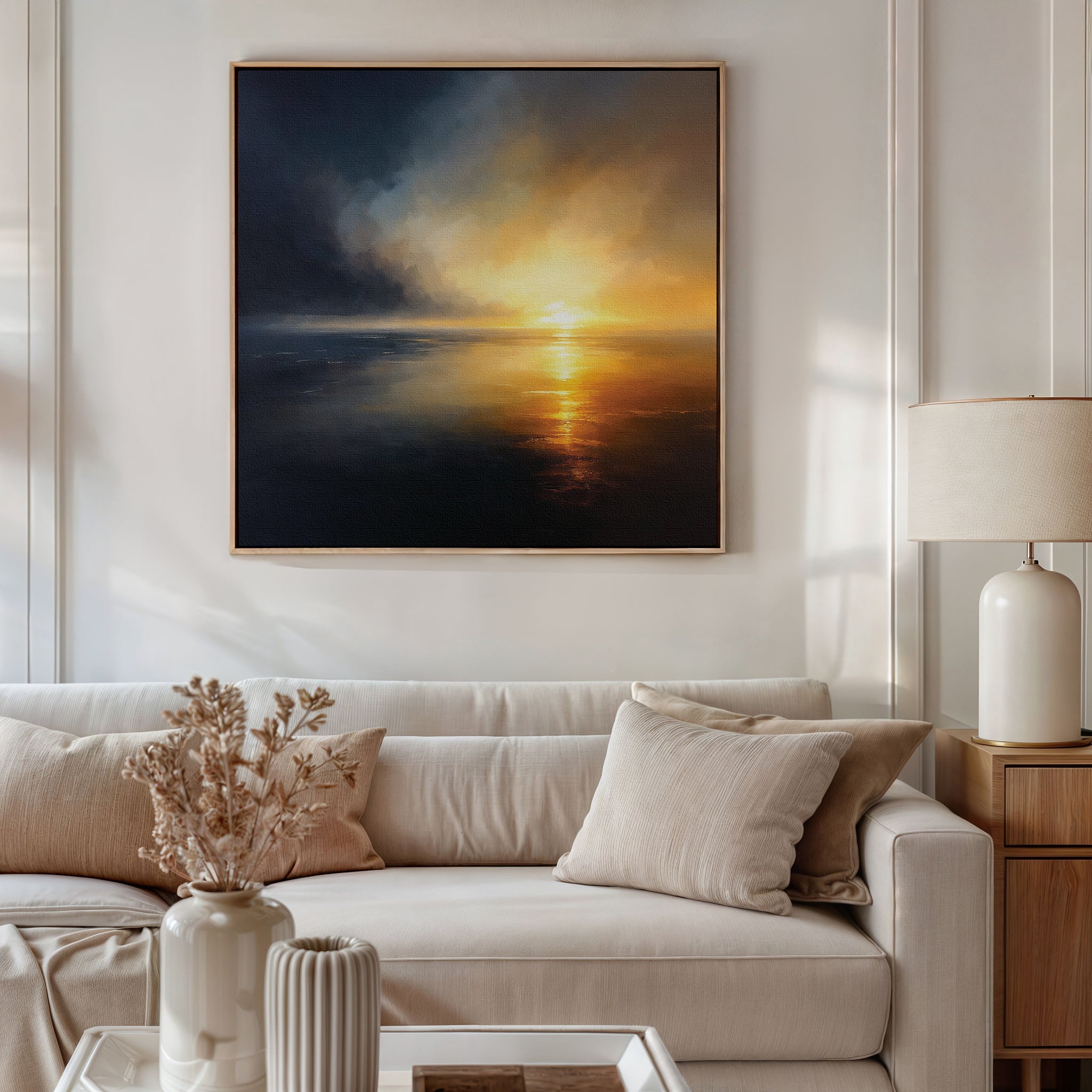 A modern living room with a beige sofa, light pillows, a white lamp on a wooden side table, a vase of dried flowers, and atmospheric wall art—Storm's Edge Canvas Art - Square—displayed above the sofa.