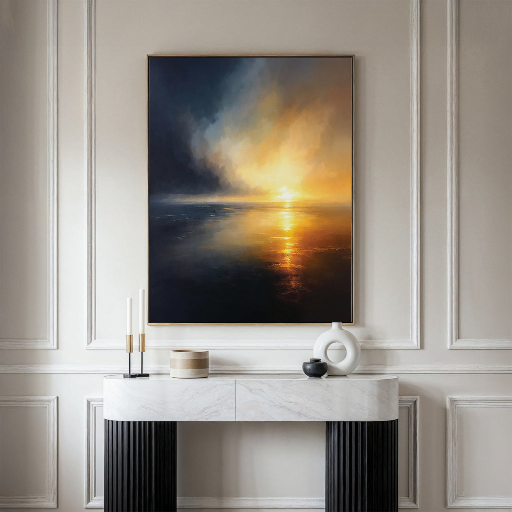 A minimalist console table with decor sits against a paneled wall, above which hangs the Storm's Edge Canvas Art - Vertical, a striking print featuring a dramatic sunset over water in deep blue, orange, and yellow tones.