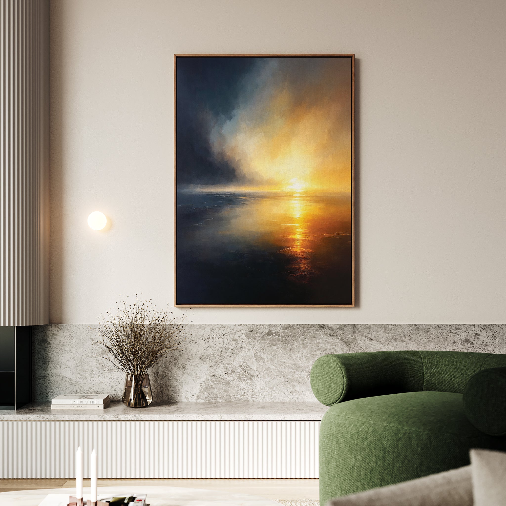 A modern living room with a green curved sofa, marble-topped bench, and atmospheric Storm's Edge Canvas Art - Vertical depicting a dramatic sunset over water. A vase with dried branches and two white candles sit on the bench.