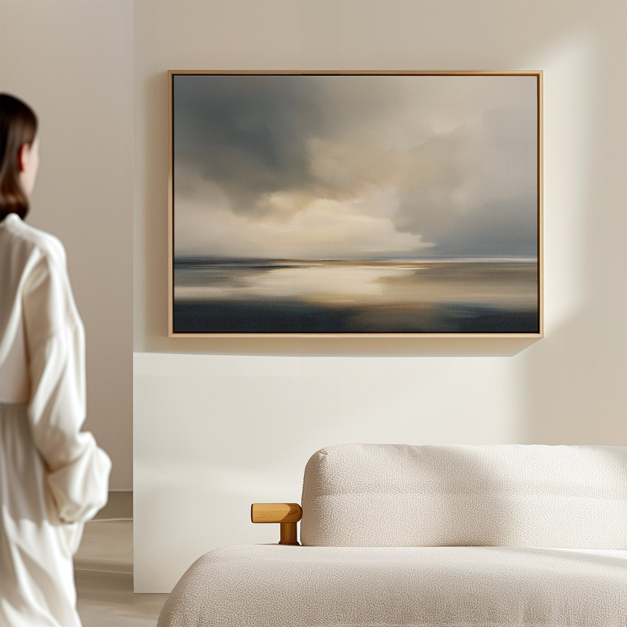 A person stands in a modern, minimal room admiring the Stormy Tides Canvas Art - Horizontal with soft, muted colors, hung on a light wall above a beige sofa.