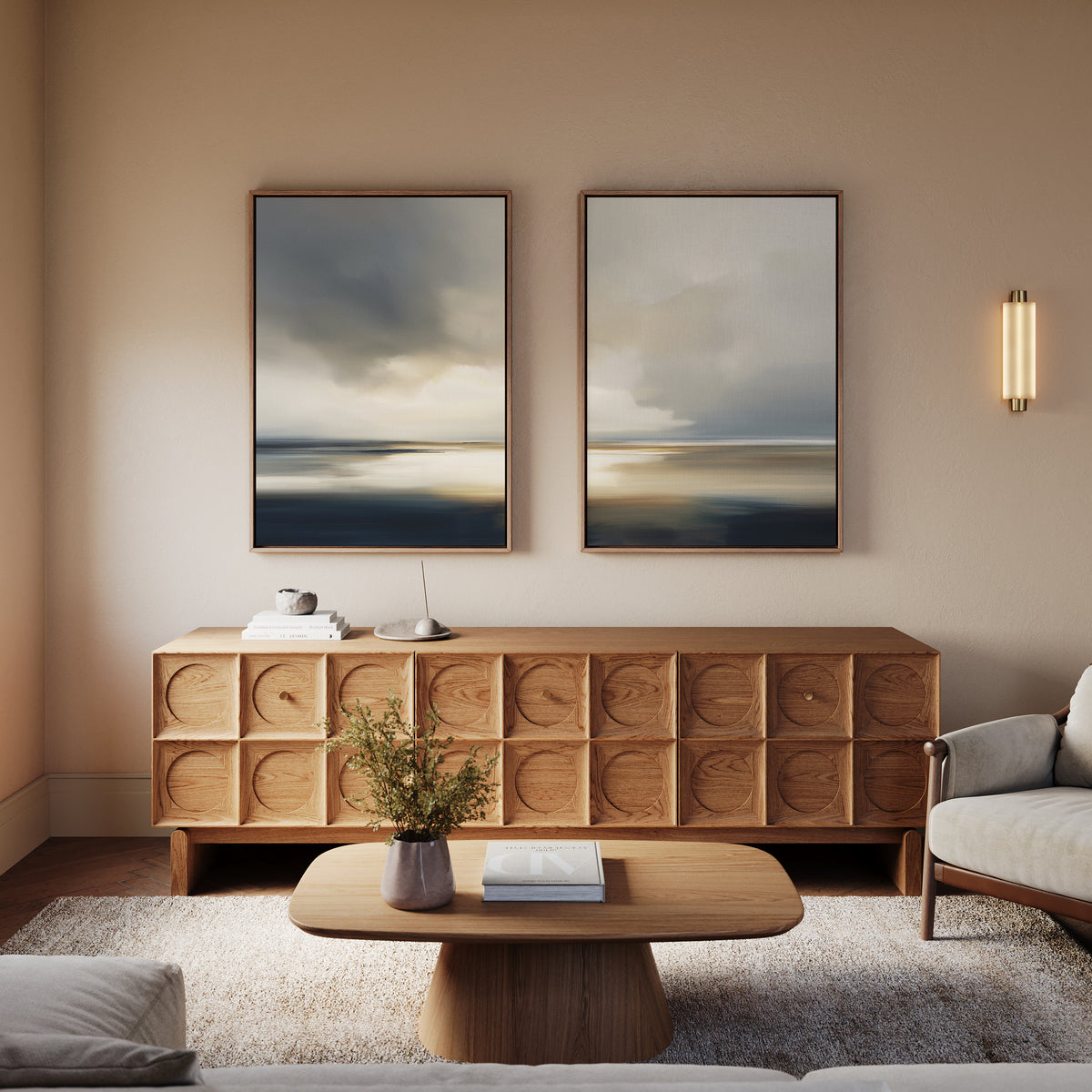 A modern living room featuring the Stormy Tides - Set Of 2 coastal wall art, a wooden sideboard and coffee table, a small plant, books, decorative object, neutral-toned sofa, and soft wall lighting for a calm, minimalist vibe.