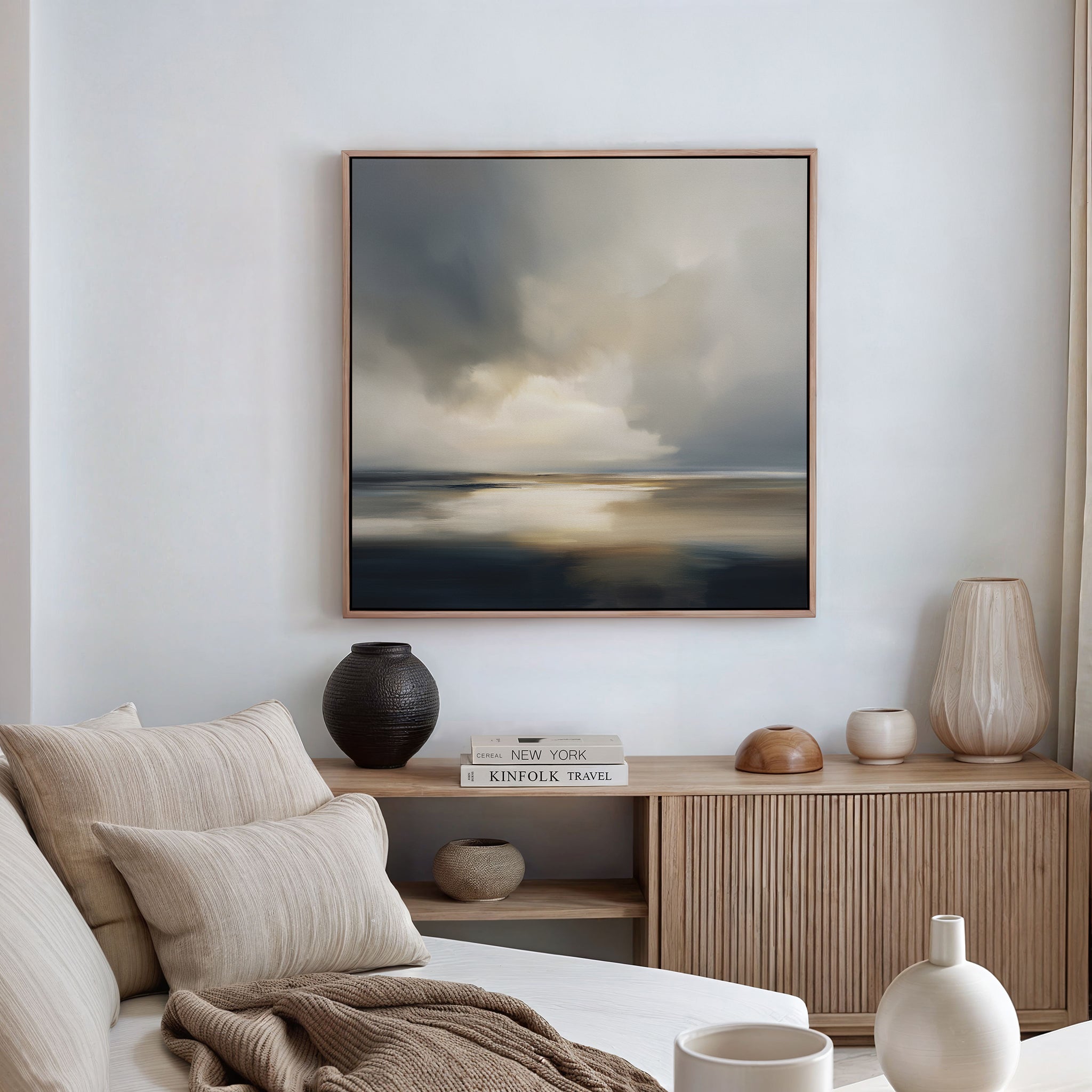 A cozy, modern living room with a beige sofa, neutral cushions, a wooden sideboard adorned with vases and books, and the Stormy Tides Canvas Art - Square, inspired by Nordic Park, creating a striking focal point on the wall.
