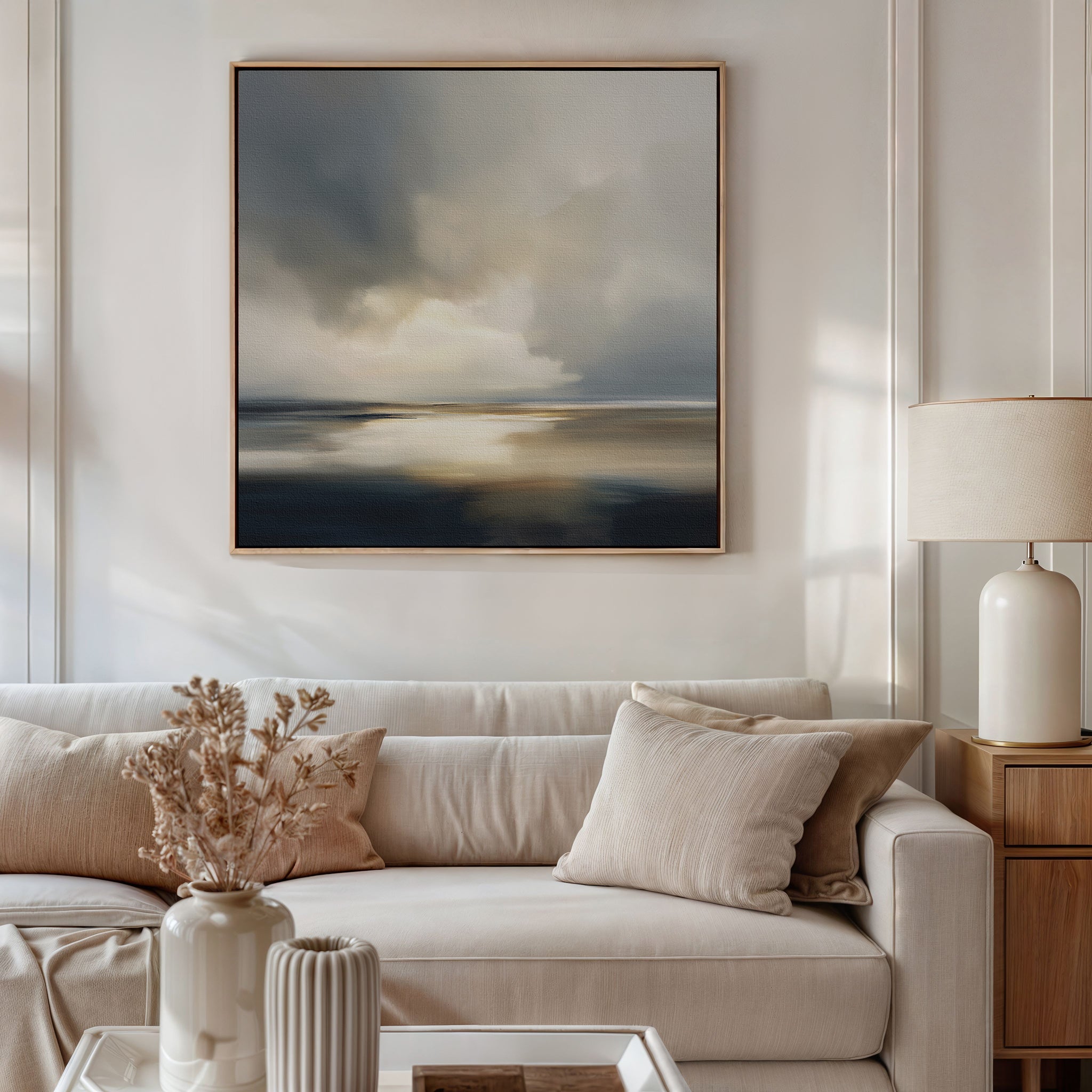 A modern living room with a beige sofa, neutral-toned pillows, a ceramic vase with dried flowers on the coffee table, a table lamp, and Stormy Tides Canvas Art - Square above the sofa creates a serene and stylish space.