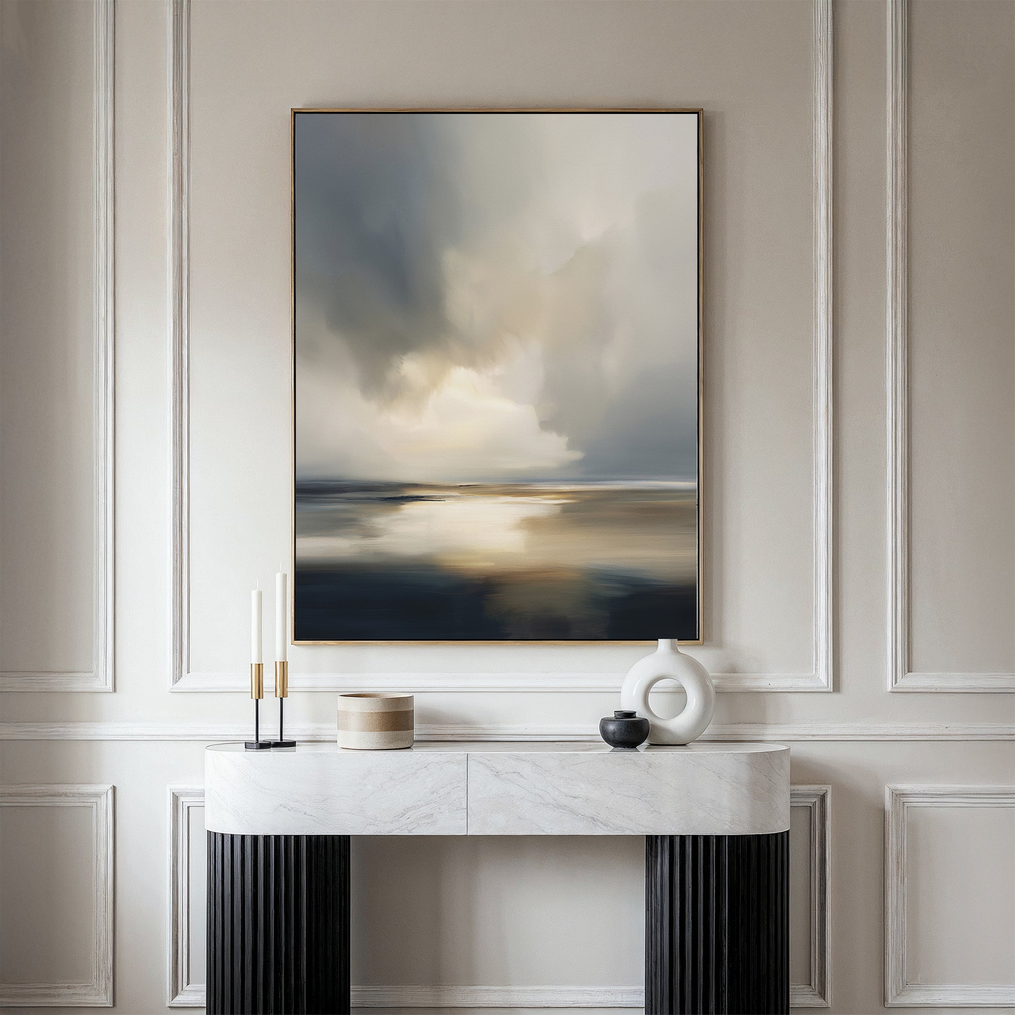 A modern console table with black legs and a white marble top stands against a cream wall. On the table are decorative objects, while above it hangs the Stormy Tides Canvas Art - Vertical in soft, muted gray, blue, and beige tones.