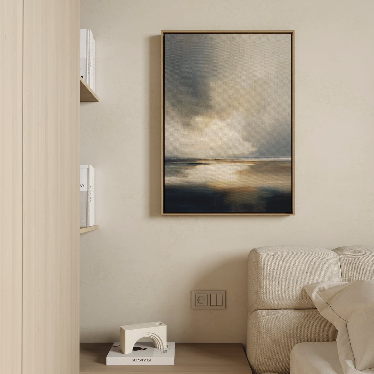 A minimalist living room features a beige sofa, light wooden bookshelves, and the Stormy Tides Canvas Art - Vertical, showcasing soft blue, beige, and white tones for a serene coastal atmosphere.