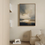 A minimalist living room features a beige sofa, light wooden bookshelves, and the Stormy Tides Canvas Art - Vertical, showcasing soft blue, beige, and white tones for a serene coastal atmosphere.