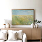 A light wood sideboard with white vases and a lamp sits against the wall. Above, the vintage decor is highlighted by the Summers Embrace Canvas Art, featuring a grassy field under a blue sky. A beige sofa with white cushions is in front.