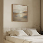 A modern beige bedroom with a low upholstered bed, white bedding, and three pillows. Above the bed hangs the Sunlit Waters Canvas Art - Square print. A twig in a vase decorates the right bedside table.