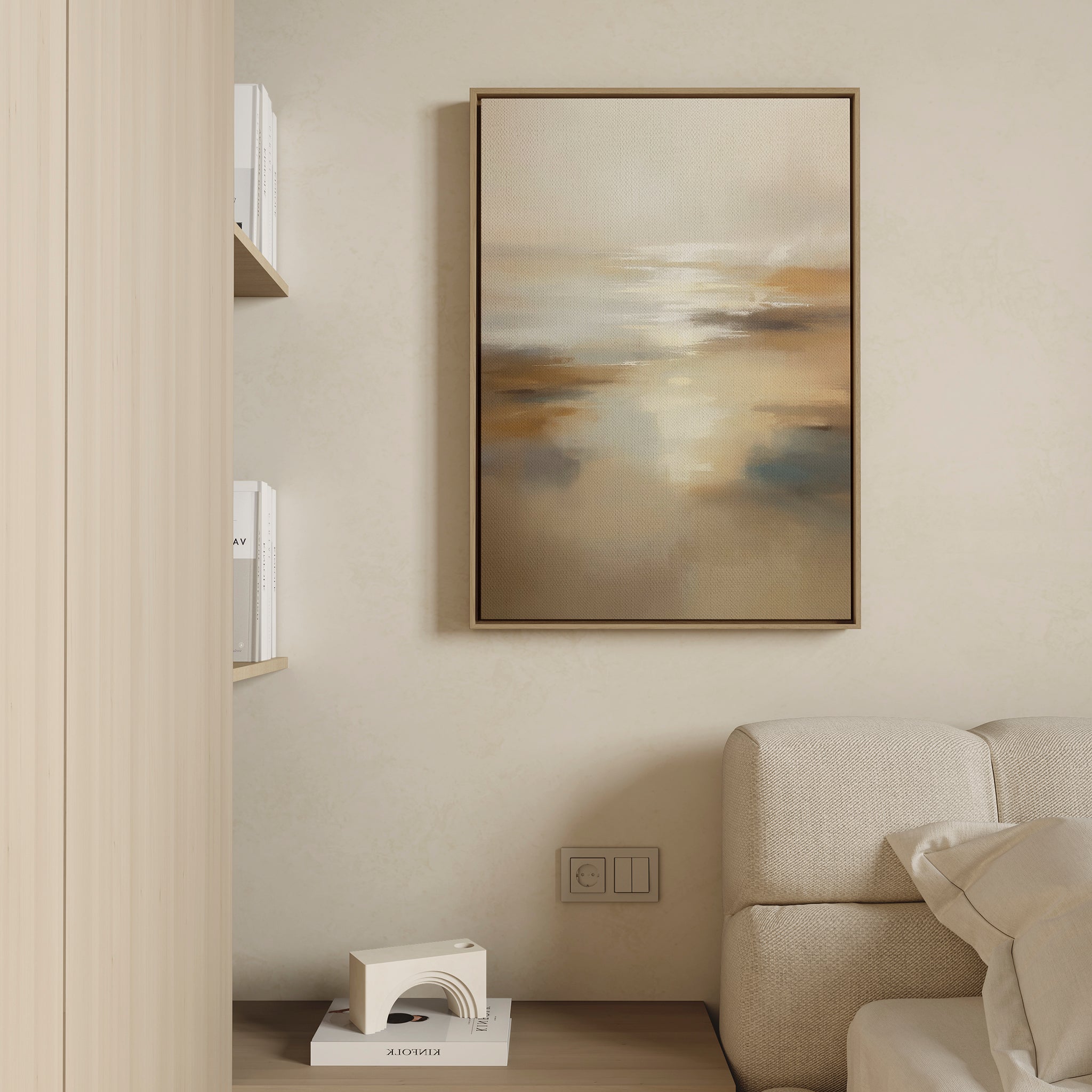 A beige, minimalist living room corner with a white textured sofa, a shelf with books, a geometric decor piece, and the Sunlit Waters Canvas Art - Vertical in warm neutral tones displayed on the wall.