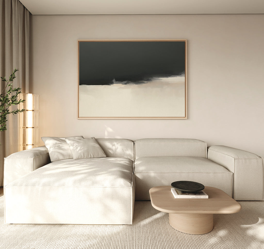 A modern living room with a light beige sectional sofa, low wooden coffee table with a dark bowl, tall plant, neutral curtains, and Tempest Brewing Canvas Art - Horizontal on the wall featuring dramatic dark and light tones.