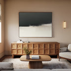 A modern living room with a wooden sideboard featuring circular patterns, Tempest Brewing Canvas Art - Horizontal above it, a light wood coffee table, beige sofa, small plant on the table, and soft neutral decor.