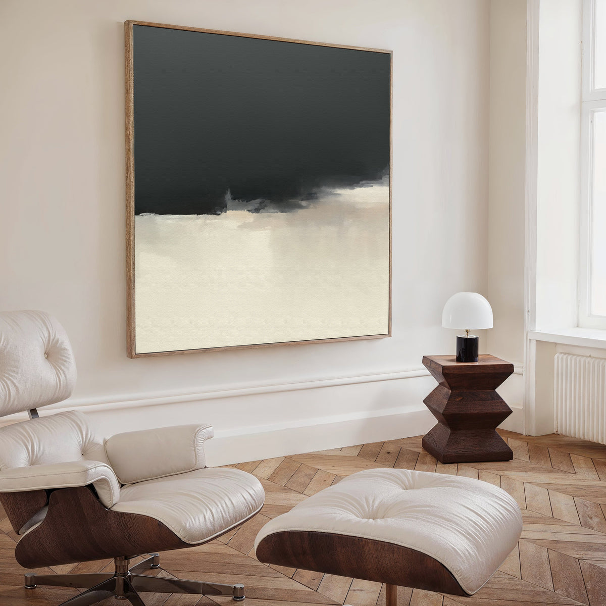 A modern minimal living room with a white leather lounge chair and ottoman, wooden side table with lamp, and the Tempest Brewing Canvas Art - Square in neutral tones displayed above herringbone wood floors.