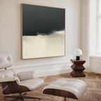 A modern minimal living room with a white leather lounge chair and ottoman, wooden side table with lamp, and the Tempest Brewing Canvas Art - Square in neutral tones displayed above herringbone wood floors.