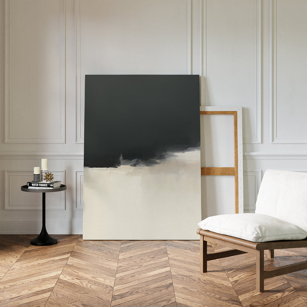 A modern minimalist room with the Tempest Brewing Canvas Art - Vertical leaning against a white paneled wall, a round black side table with candles, and a cushioned wooden chair on a herringbone wood floor.