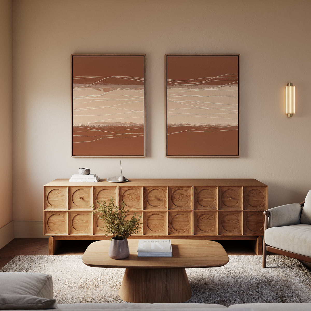 A cozy living room features a wooden sideboard, a low coffee table, a light-colored sofa, Terracotta Currents - Set Of 2 wall art, a small wall sconce, and a vase with greenery for modern elegance.