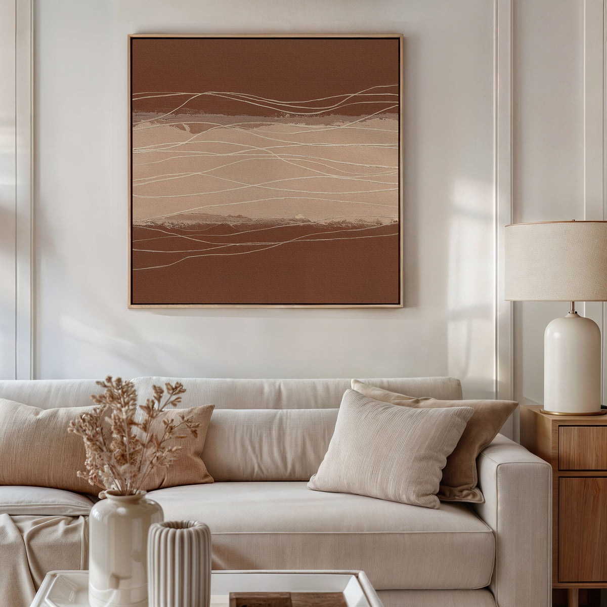 A modern living room with a beige sofa, neutral pillows, and Nordic Park-themed decor features the Terracotta Currents Canvas Art - Square in brown and beige tones. A wooden side table, white lamp, and vase with dried flowers complete the look.