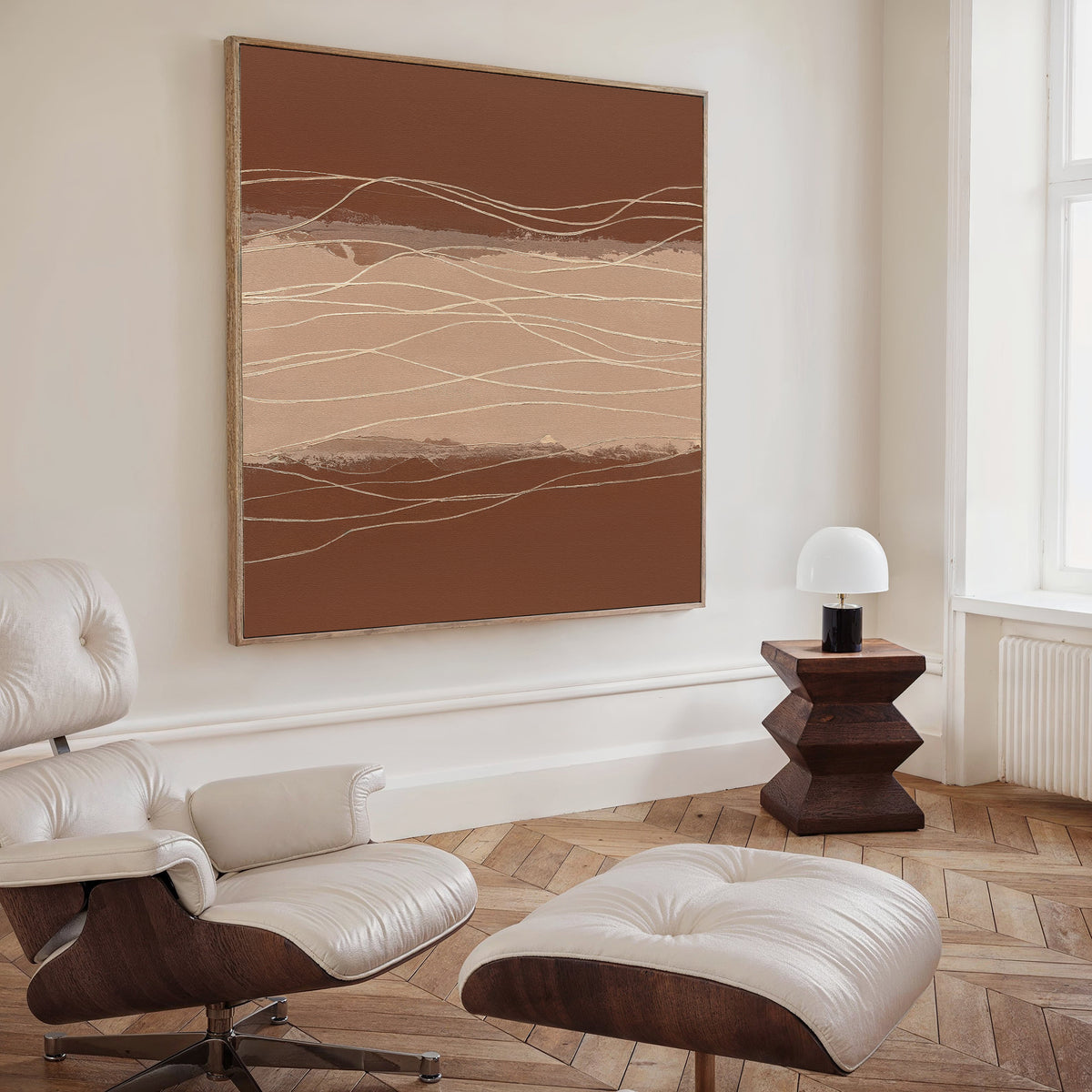 A modern living room with a white leather lounge chair and ottoman, a geometric wooden side table with a white lamp, and the Terracotta Currents Canvas Art - Square in brown and beige tones, adding Nordic Park-inspired style to the space.
