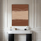 A modern entryway features a white marble console table, minimalist decor, and the Terracotta Currents Canvas Art - Vertical with wavy lines and earth tones on a paneled wall.