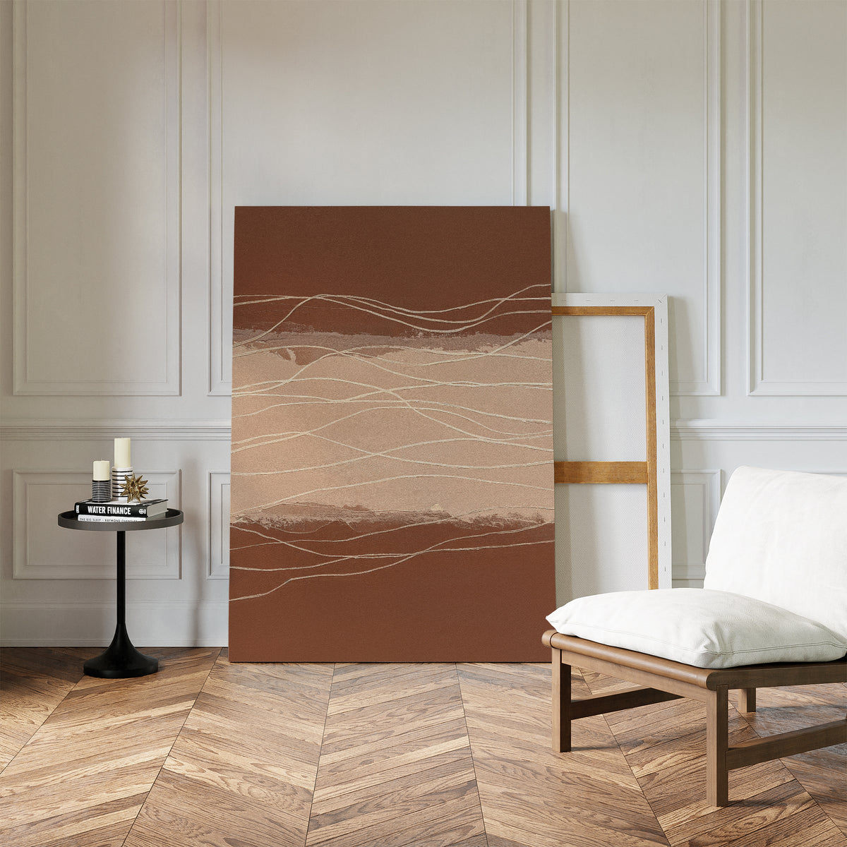 A minimalist room with white paneled walls, herringbone wood floors, a cushioned chair, and a small black table holds candles and books. The Terracotta Currents Canvas Art - Vertical leans against the wall, adding warmth to the serene space.